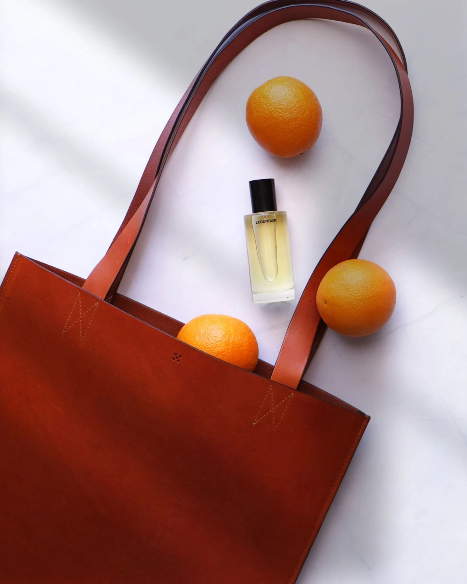 Legendär Tote Bag aus Leder mit Orangen und Eau de Parfum auf hellem Untergrund arrangiert
